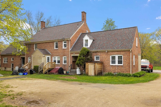 rear view of house featuring a chimney, roof with shingles, and brick siding