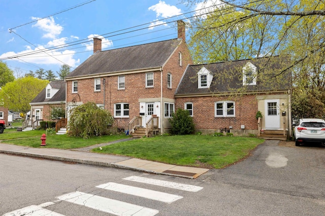 view of front of house featuring roof with shingles, a chimney, a front lawn, and brick siding