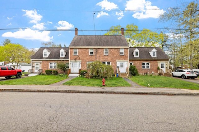 view of front facade with a front yard, brick siding, a chimney, and entry steps