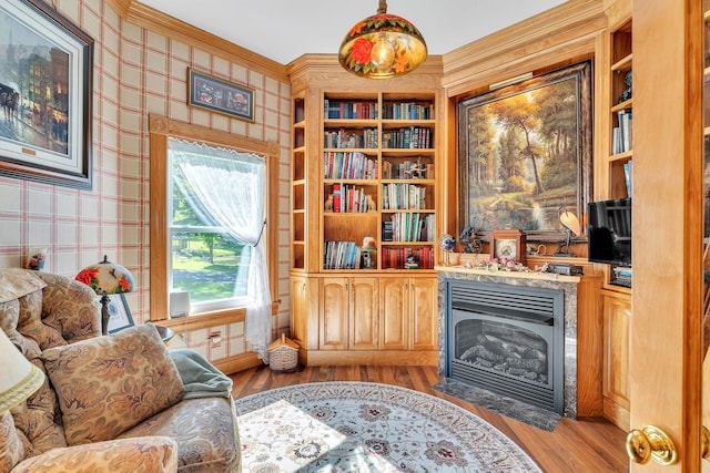 sitting room featuring built in shelves, light wood finished floors, crown molding, a fireplace with flush hearth, and wallpapered walls