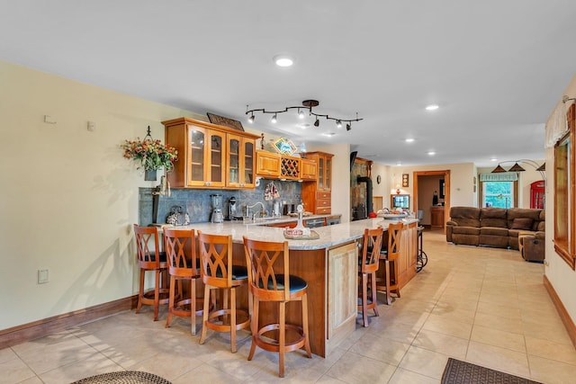 kitchen with a peninsula, backsplash, light tile patterned floors, glass insert cabinets, and baseboards