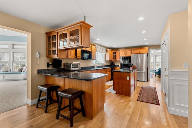 8 Palis Dr, Salisbury, MA 01952 - kitchen featuring a toaster, brown cabinetry, a peninsula, black appliances, and light wood-type flooring