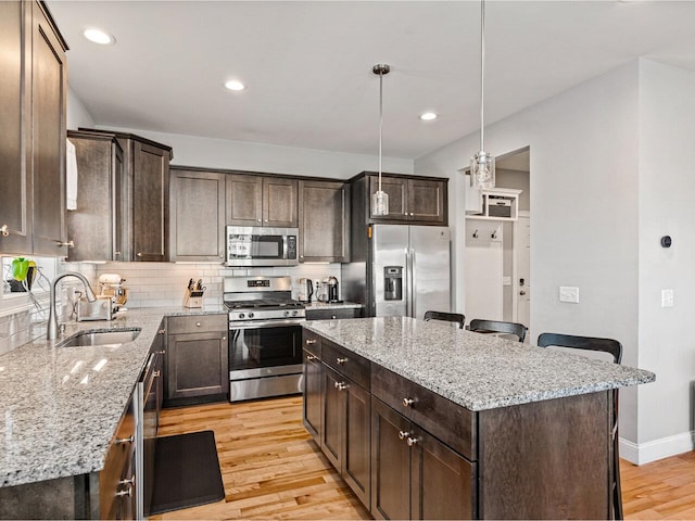 kitchen with a center island, a sink, appliances with stainless steel finishes, dark brown cabinetry, and light wood-style floors