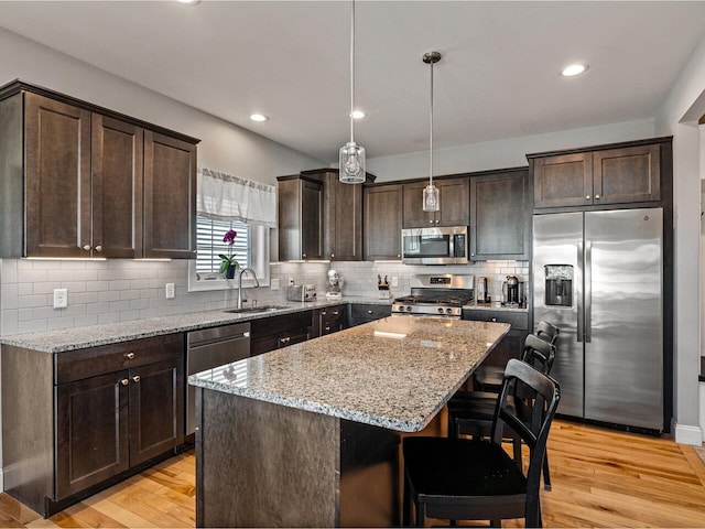 kitchen featuring light stone counters, appliances with stainless steel finishes, a sink, and dark brown cabinetry