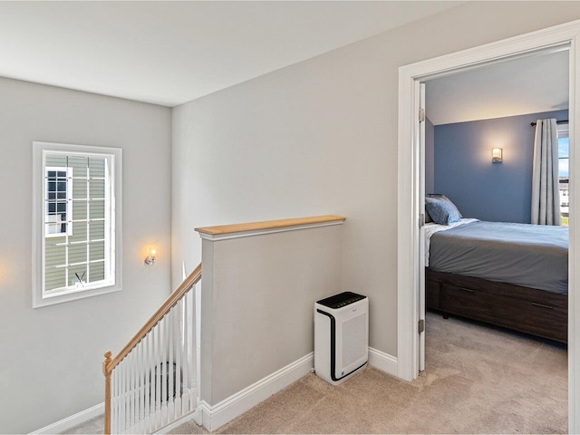 corridor with light colored carpet, a wealth of natural light, an upstairs landing, and baseboards