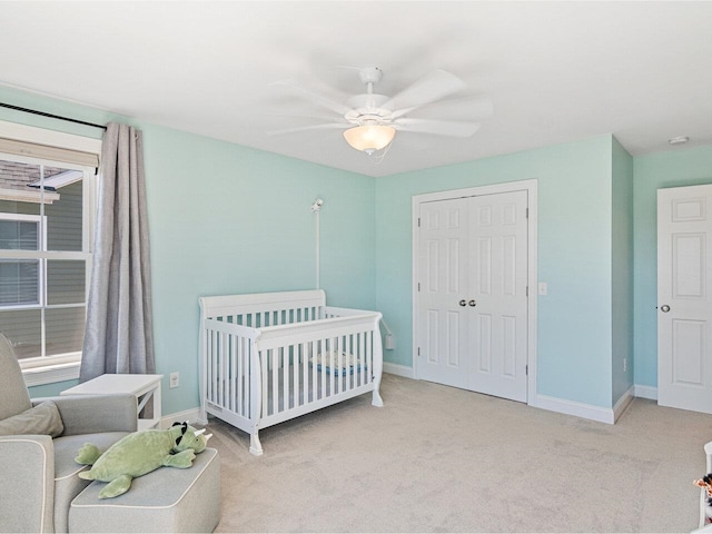 carpeted bedroom with a crib, a closet, baseboards, and a ceiling fan