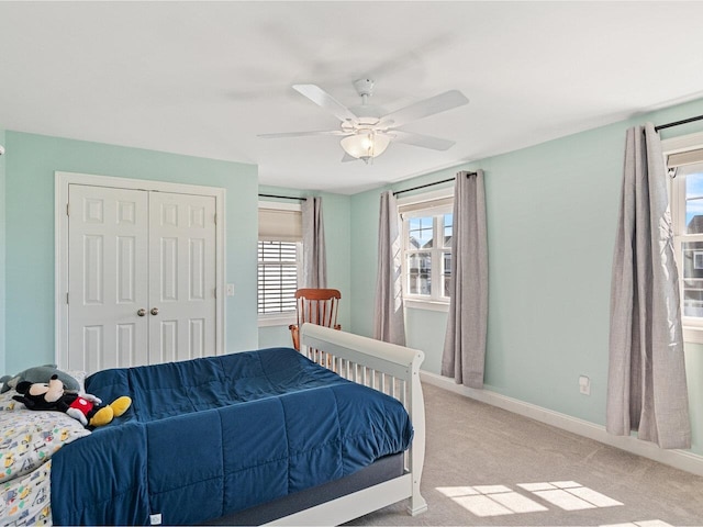 bedroom featuring multiple windows, a closet, baseboards, and light carpet