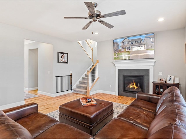 living room with a tile fireplace, wood finished floors, a ceiling fan, baseboards, and stairs