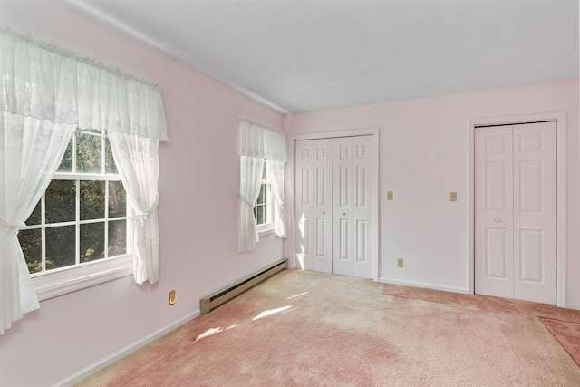 unfurnished bedroom with carpet flooring, baseboards, a baseboard radiator, and multiple closets