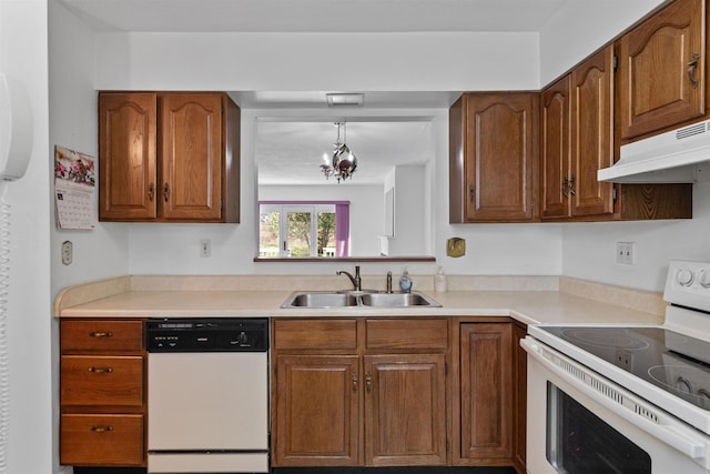 kitchen with a sink, white appliances, under cabinet range hood, and brown cabinets