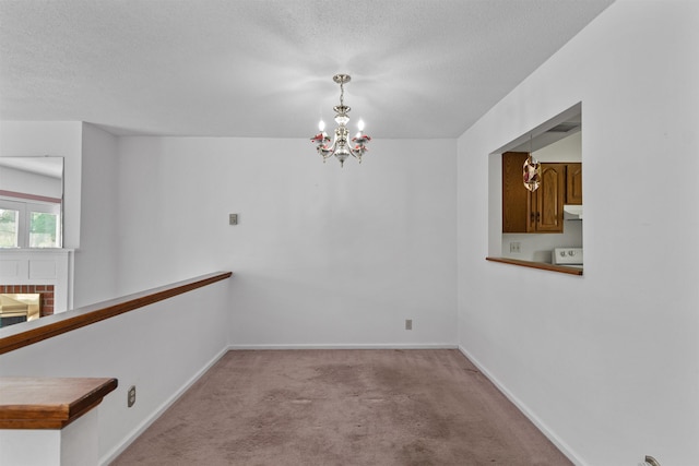 carpeted empty room featuring an inviting chandelier, a textured ceiling, and baseboards