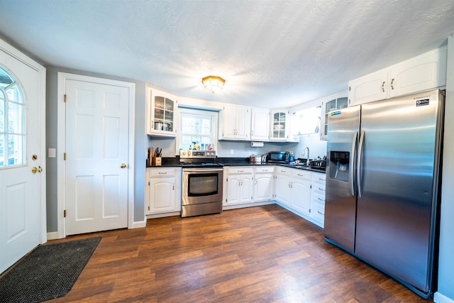 kitchen featuring a sink, glass insert cabinets, white cabinets, dark countertops, and appliances with stainless steel finishes