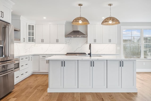 kitchen featuring a sink, wall chimney range hood, high end fridge, recessed lighting, and white cabinets