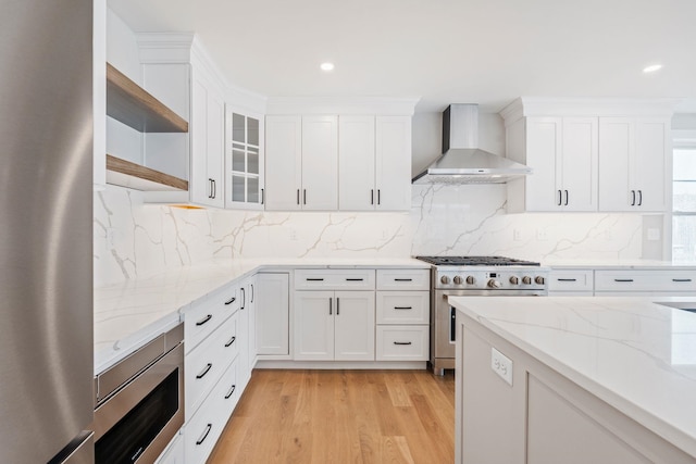 kitchen with white cabinets, stainless steel appliances, light wood-type flooring, and wall chimney exhaust hood