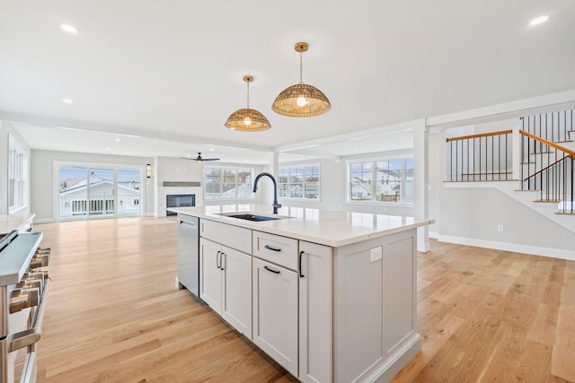 kitchen with a sink, open floor plan, light wood-style floors, stainless steel appliances, and an island with sink