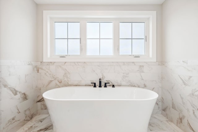 full bath with wainscoting, a freestanding bath, tile walls, and marble finish floor