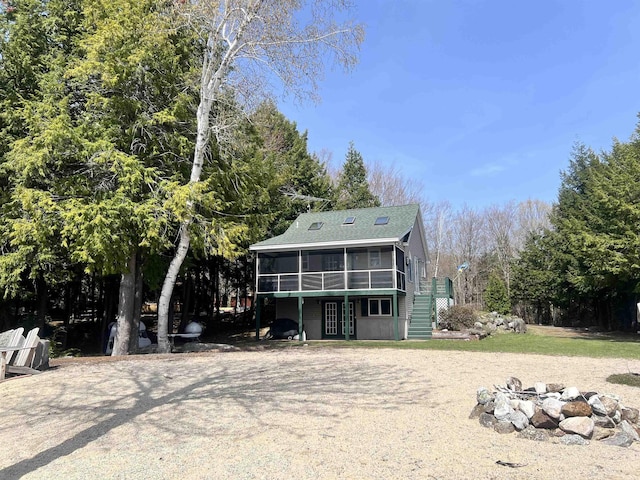 back of property featuring driveway, french doors, an outdoor fire pit, a sunroom, and a shingled roof
