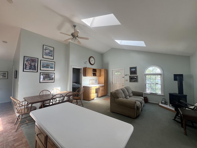 carpeted living area with a wood stove, lofted ceiling with skylight, and a ceiling fan