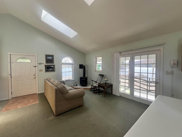 carpeted living area with a wood stove, a skylight, and high vaulted ceiling