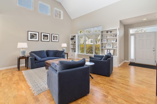living area with baseboards, a wealth of natural light, light wood-type flooring, and high vaulted ceiling