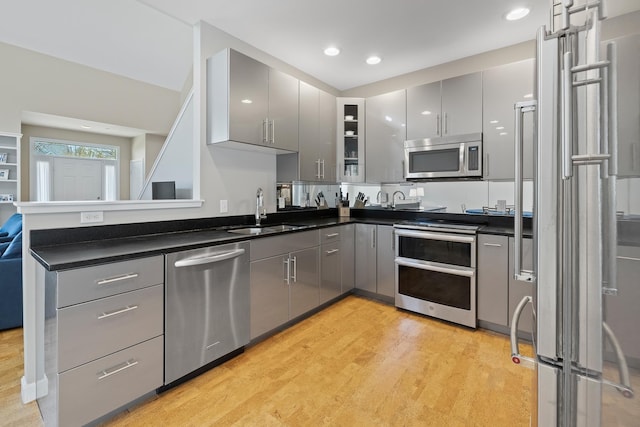 kitchen with light wood finished floors, a sink, dark countertops, appliances with stainless steel finishes, and gray cabinets