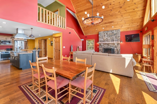 dining room featuring wood finished floors, high vaulted ceiling, wooden ceiling, a chandelier, and a stone fireplace