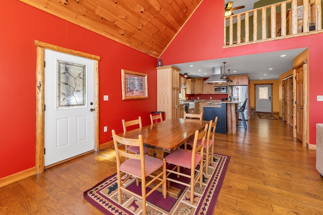 dining room featuring a ceiling fan, baseboards, light wood finished floors, and high vaulted ceiling