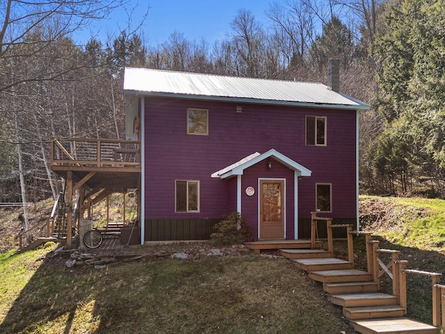 view of front of house featuring a chimney, metal roof, stairs, a deck, and a front lawn