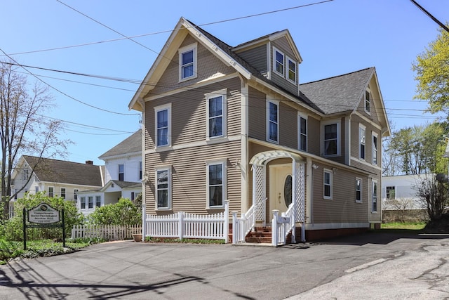 view of front facade featuring roof with shingles and fence