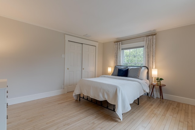 bedroom featuring light wood finished floors, a closet, baseboards, and ornamental molding