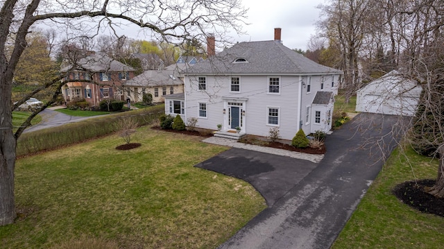 view of front of house featuring a chimney, fence, a front lawn, an outbuilding, and driveway