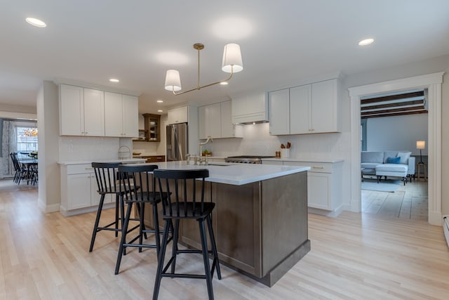 kitchen with a breakfast bar, light wood finished floors, stainless steel refrigerator with ice dispenser, backsplash, and a center island with sink