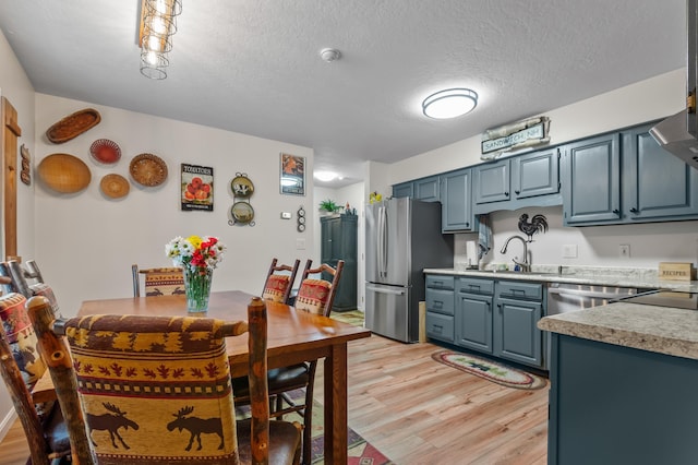 kitchen featuring stainless steel appliances, light wood finished floors, a sink, blue cabinetry, and light countertops