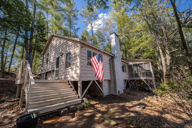 exterior space with a chimney, stairs, and a sunroom