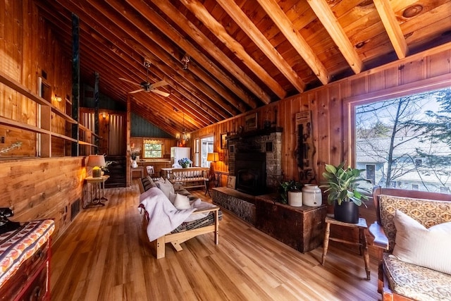living area with wooden walls, lofted ceiling with beams, a healthy amount of sunlight, and wood finished floors