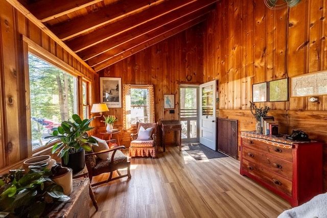 living area with wooden walls, lofted ceiling with beams, and plenty of natural light