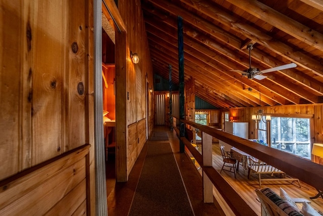 hall featuring wooden walls and vaulted ceiling with beams