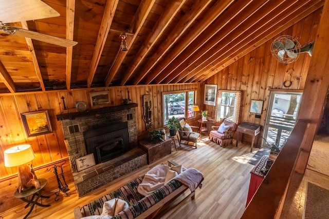 living room featuring a stone fireplace, wood ceiling, wooden walls, wood finished floors, and lofted ceiling with beams