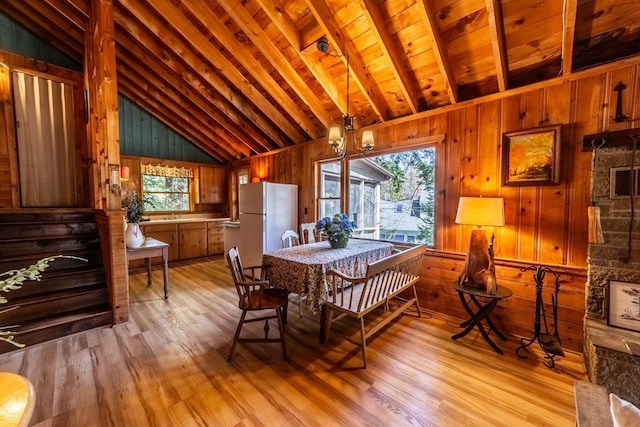 dining space with light wood finished floors, wooden walls, a wealth of natural light, and lofted ceiling with beams