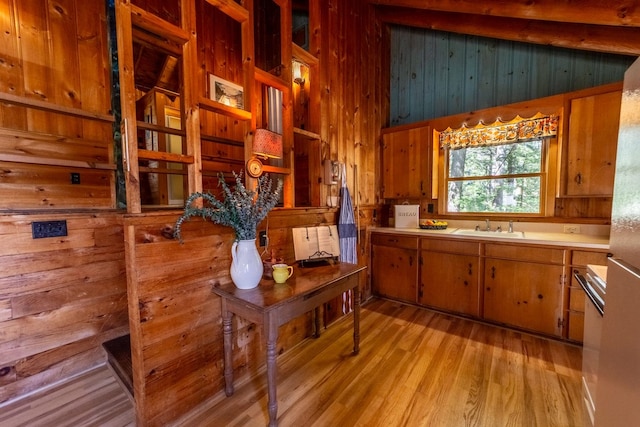 kitchen with light wood finished floors, brown cabinets, a sink, wood walls, and light countertops
