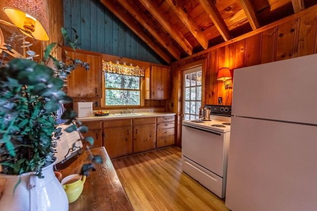 kitchen with a sink, wood walls, white appliances, and light countertops