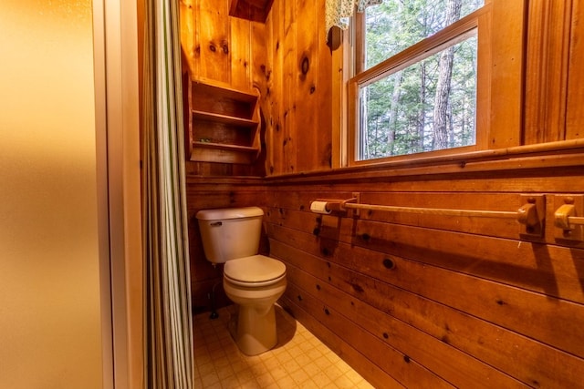 bathroom with tile patterned floors, toilet, and wooden walls