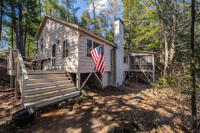 rear view of property with stairway, a sunroom, and a chimney