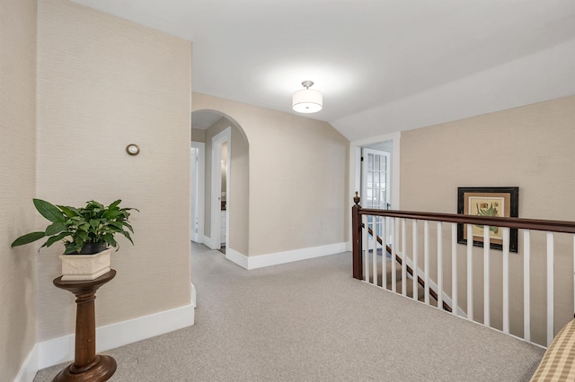 corridor with lofted ceiling, baseboards, carpet flooring, arched walkways, and an upstairs landing