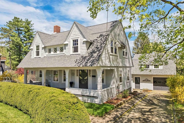 view of front facade featuring an attached garage, a chimney, concrete driveway, a porch, and roof with shingles