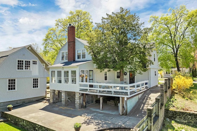 rear view of house featuring a wooden deck, a patio area, a gambrel roof, and a chimney