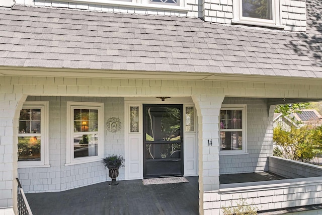 entrance to property with covered porch and a shingled roof
