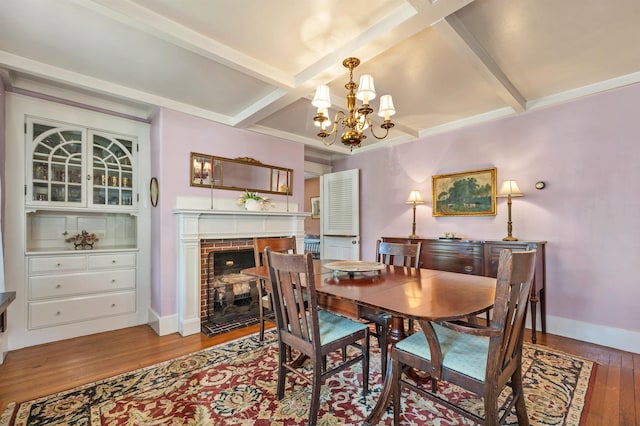 dining room featuring coffered ceiling, an inviting chandelier, hardwood / wood-style flooring, beamed ceiling, and a fireplace