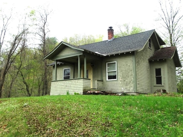 view of front of home featuring a front lawn, a porch, roof with shingles, and a chimney