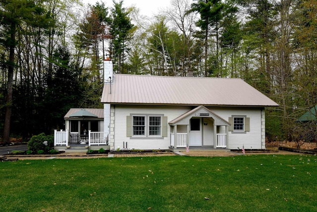 view of front of home with a porch, metal roof, a front lawn, and a chimney